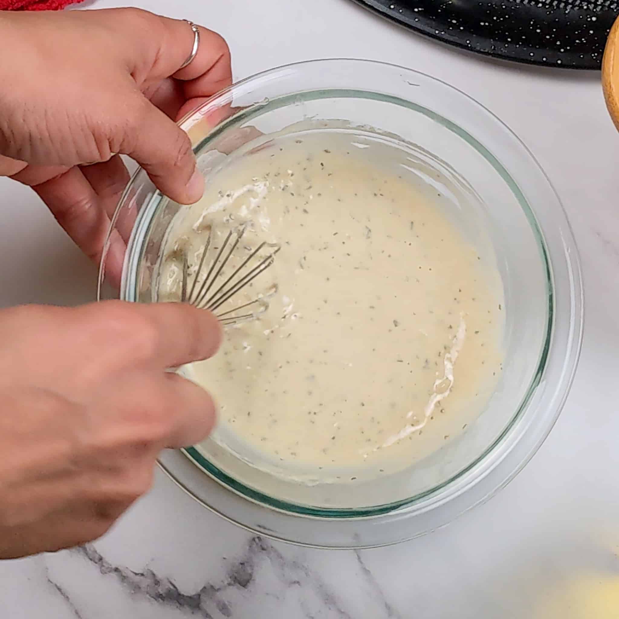 mini whisk being used to whisk the rosemary tahini dressing in a glass bowl