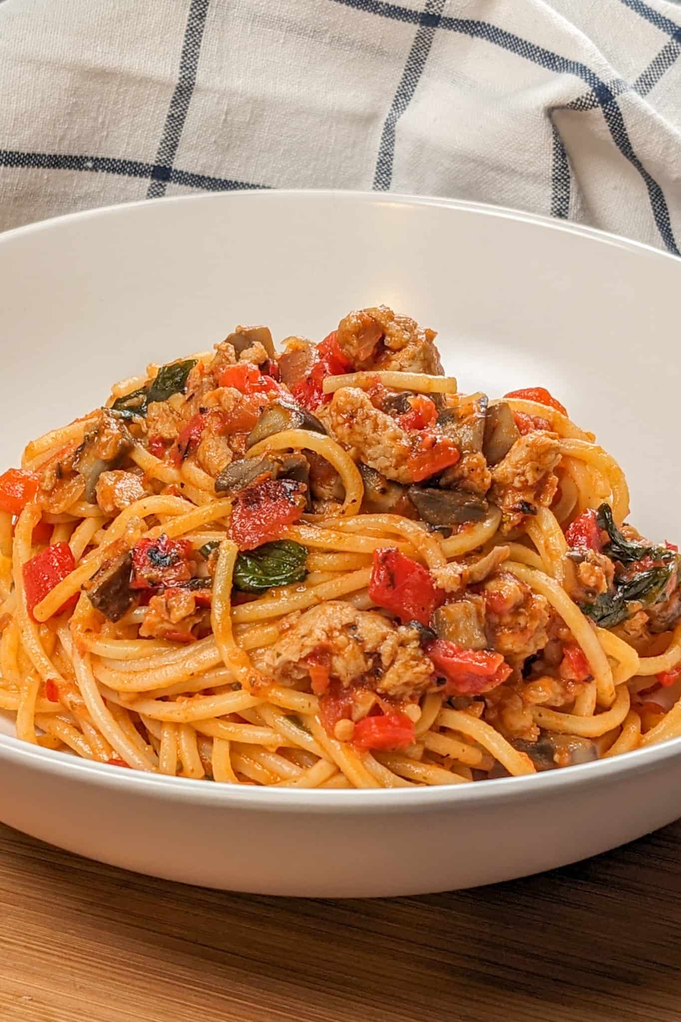 side view of the Easy Spicy Calabrian Italian Chicken Sausage Bolognese om a wide rim bowl with a kitchen towel in the background