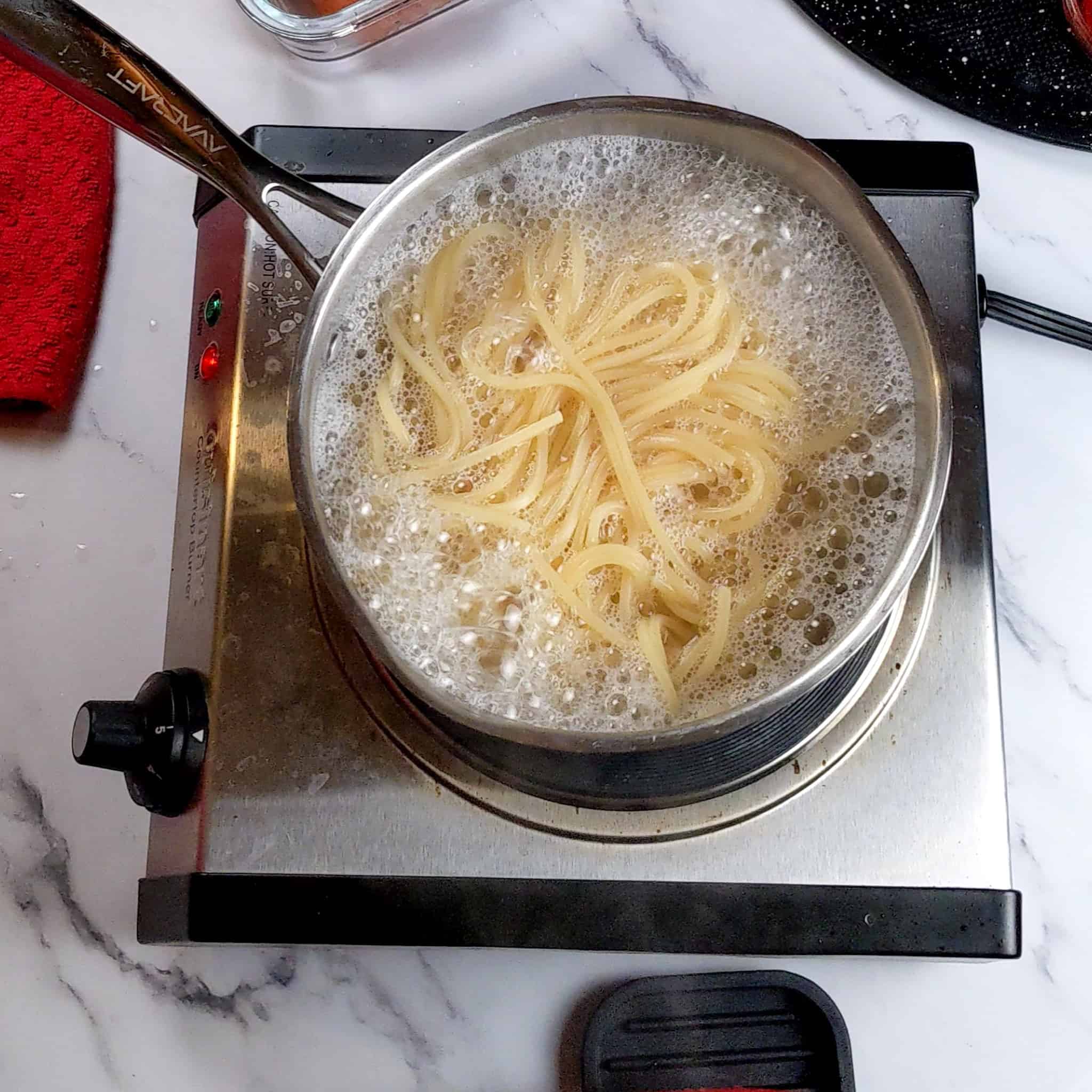 spaghetti boiling in a pot on a portable stove top