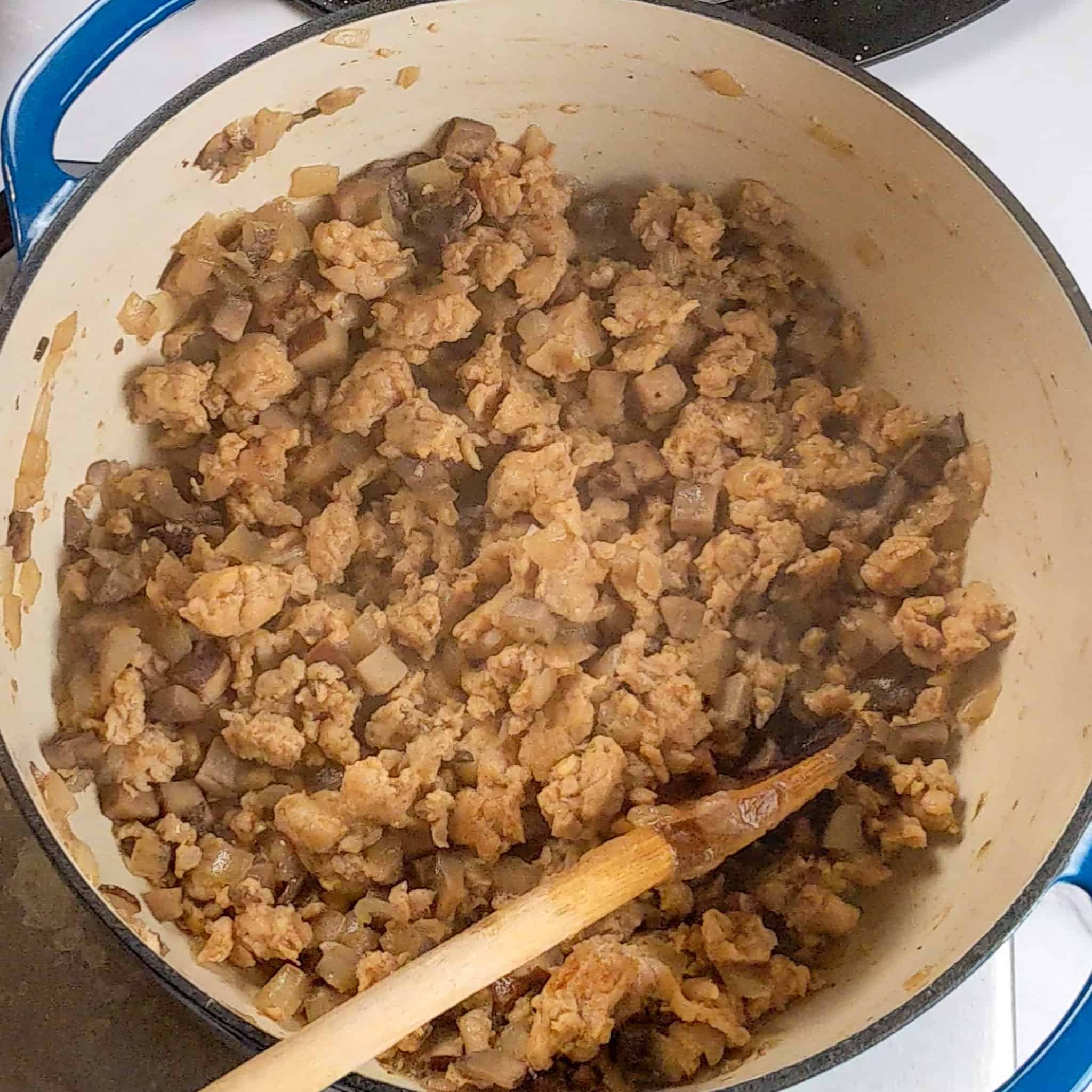 cooked crumbled sweet italian chicken sausage with cooked diced portobello mushrooms and onions in a lodge dutch oven with a wooden spoon resting inside