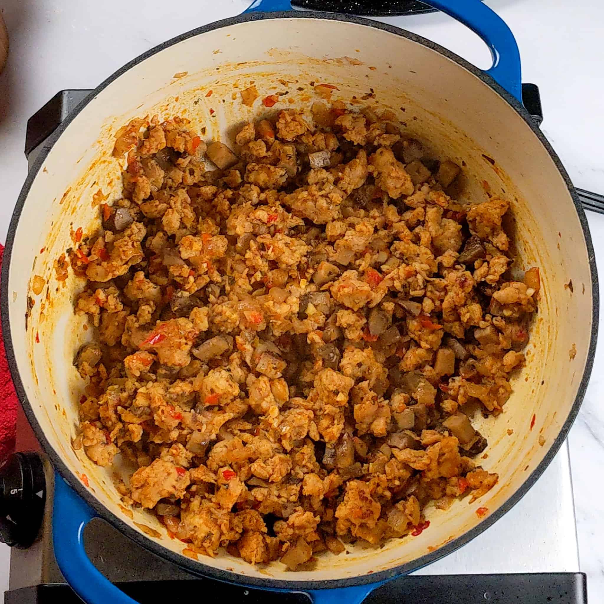 cooked crumbled sweet italian chicken sausage with diced portobello mushrooms and onions coated in crushed calabrian peppers in a lodge dutch oven