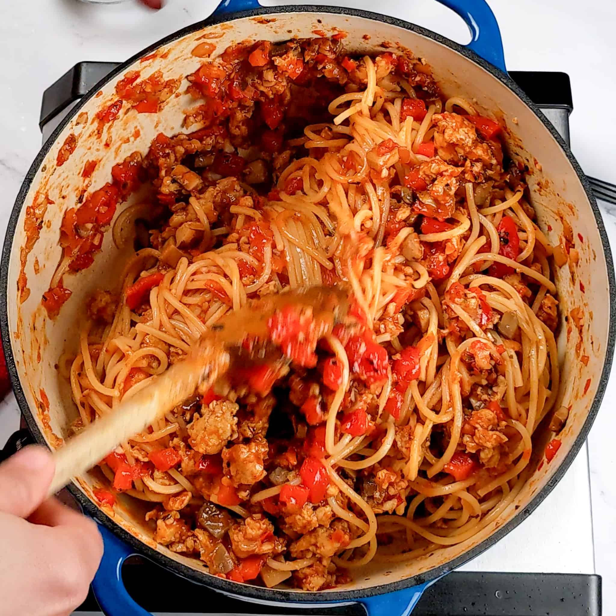 spaghetti being mixed into the chicken sausage bolognese in a pot