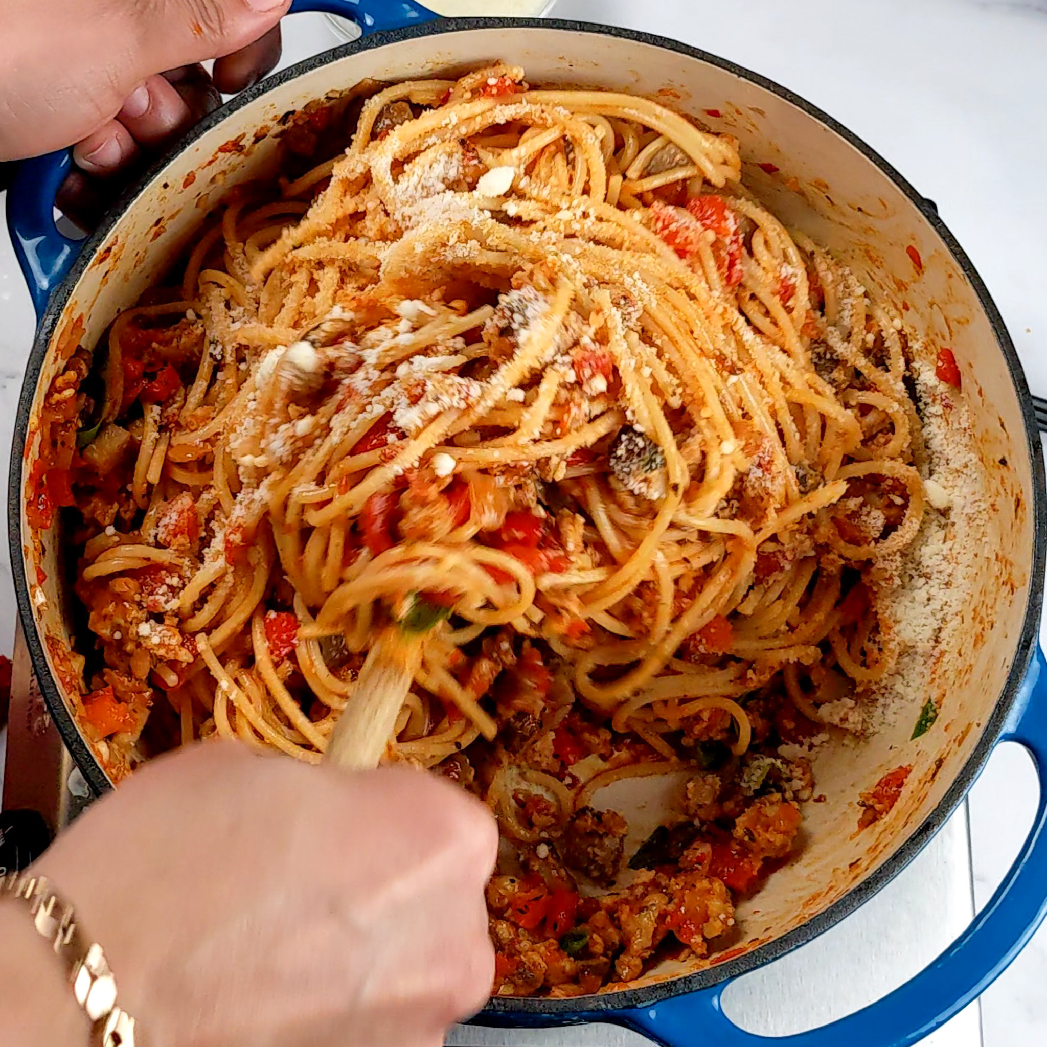 the spaghetti chicken sausage bolognese in a pot being mixed with grated pecorino cheese with a wooden spoon