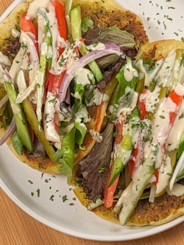 Two Spicy Falafel Pita Sandwiches with Lemon Tahini Dressing on a round white plate..