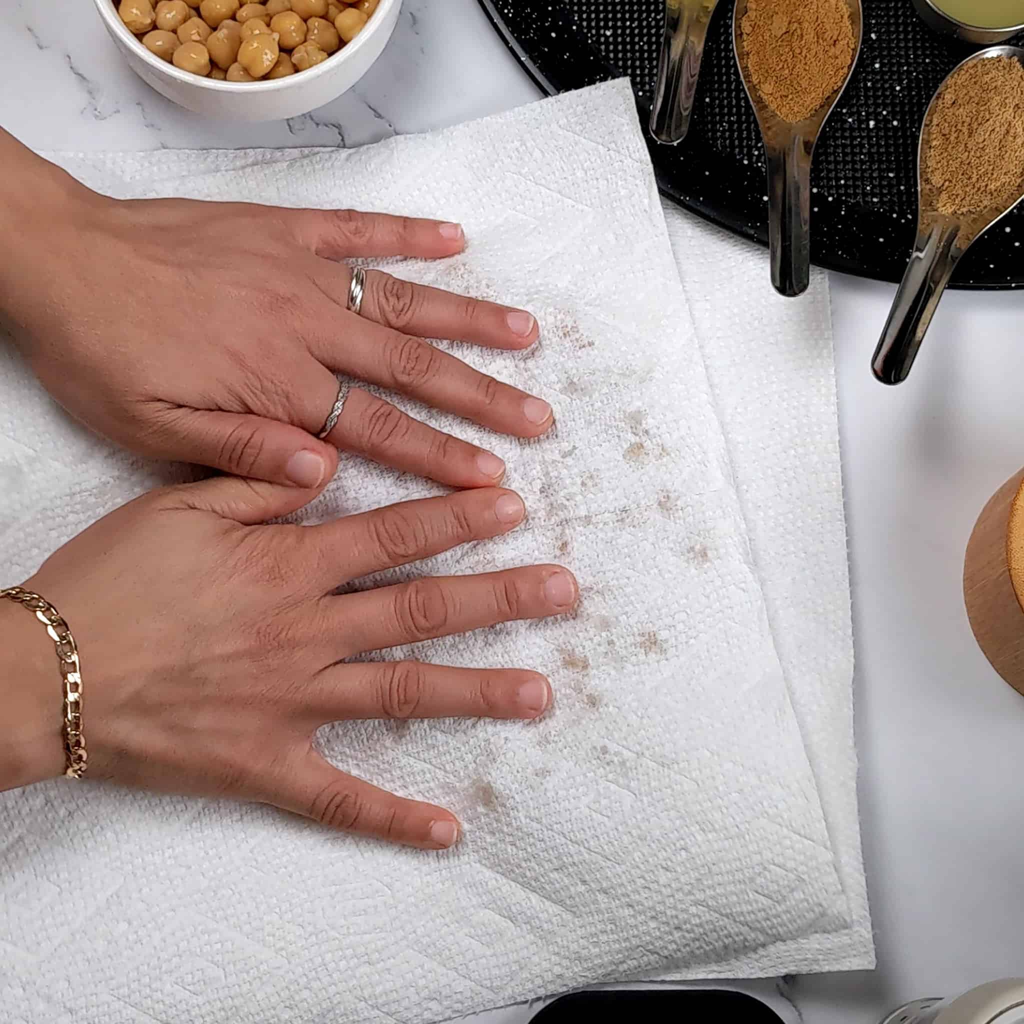 paper towel over chickpeas on a paper towel being padded down with hands