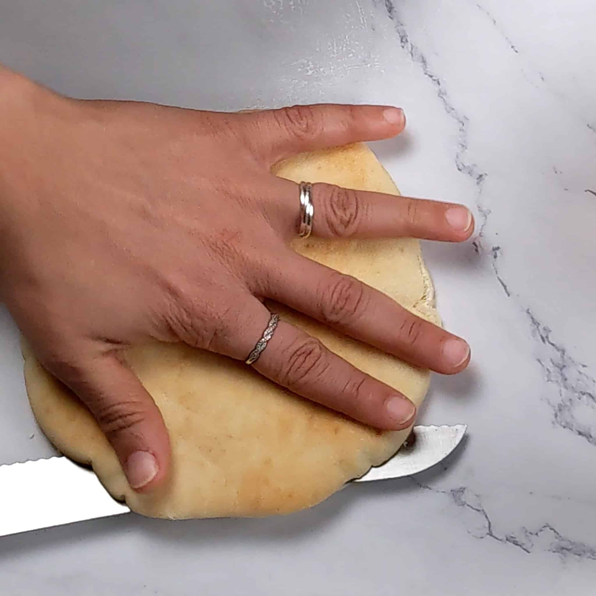 breaded knife slicing a pita in half horizontally while a hand holds it down.