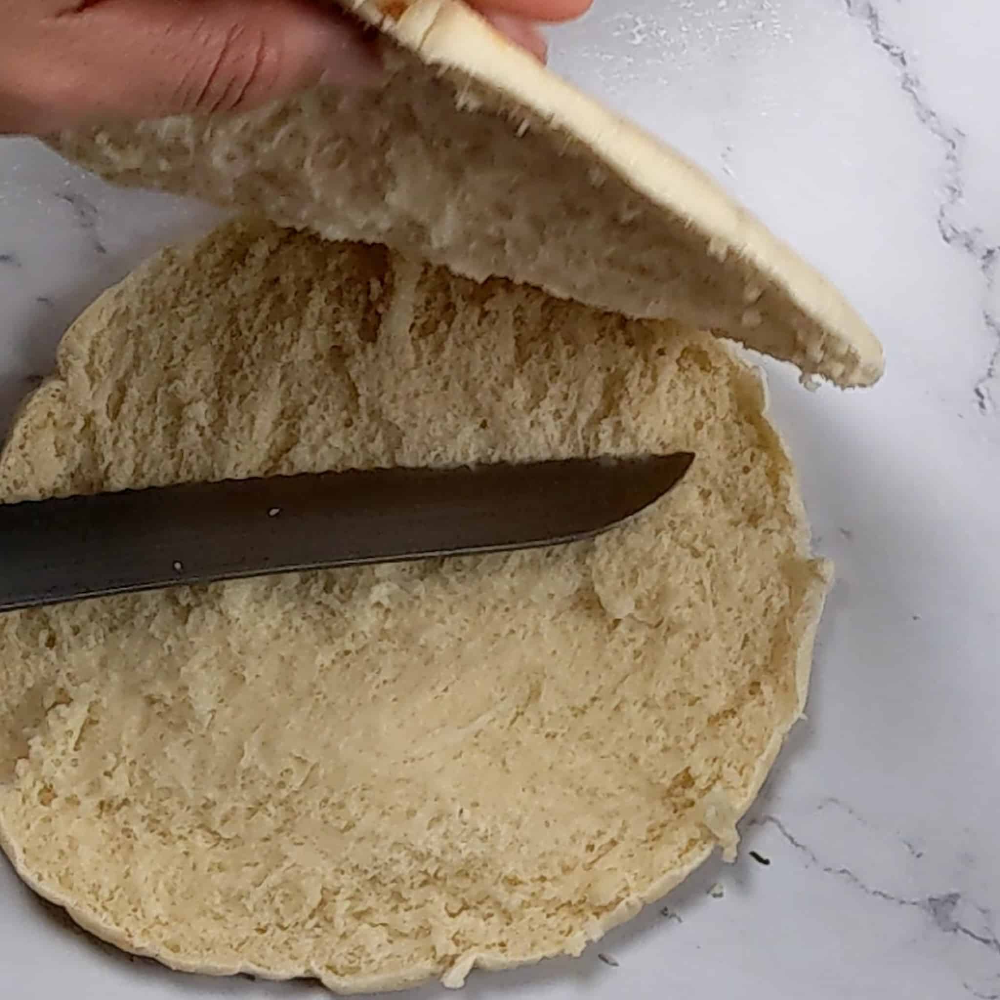 pita bread flipped open while the bread knife cuts it in half.