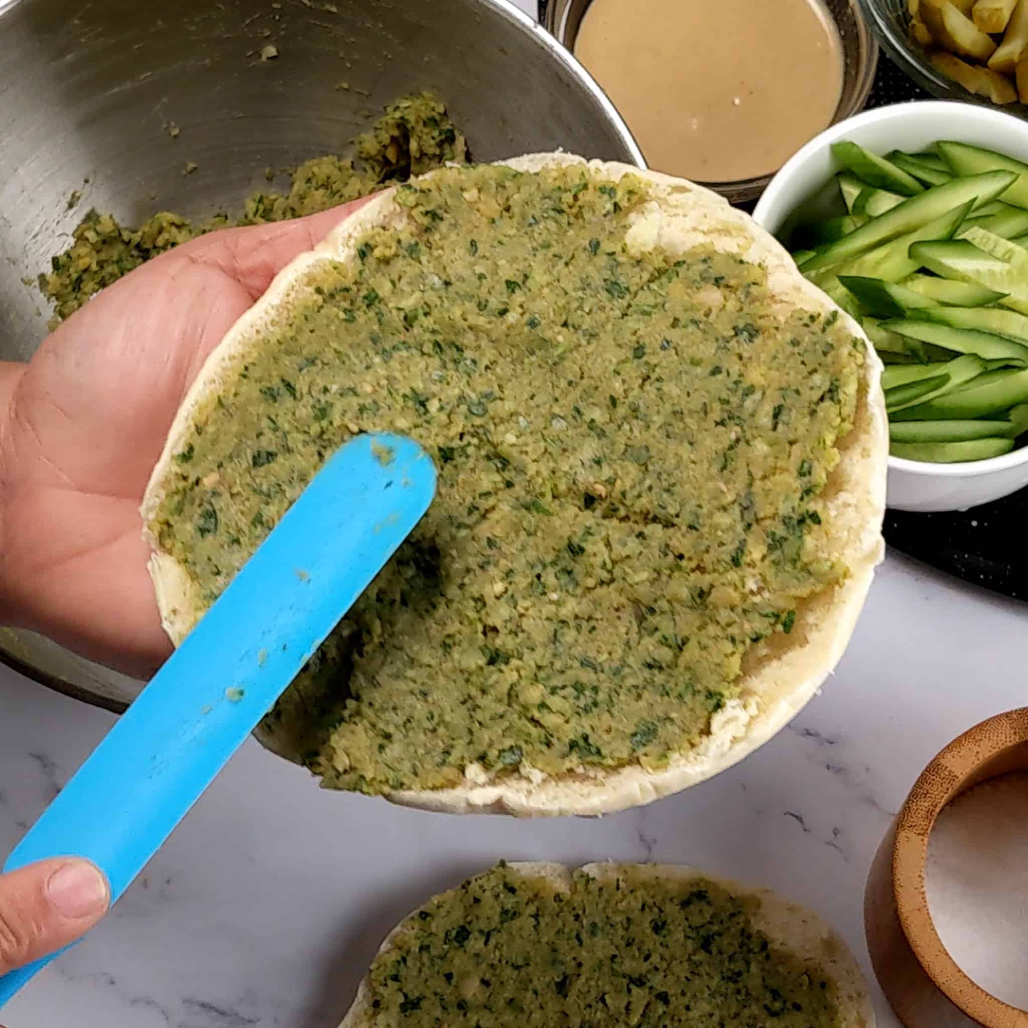 falafel mixture being spread on a pita half with a skinny silicone spatula.