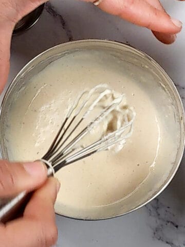 lemon tahini dressing in a small stainless steel mixing bowl with the mini spatula being lifted out.