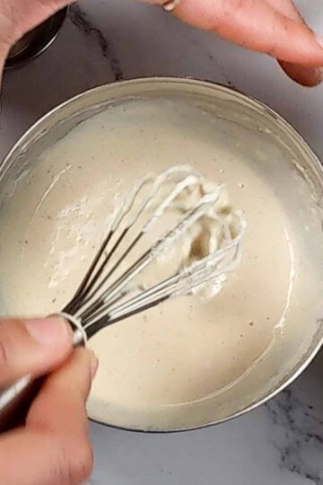 lemon tahini dressing in a small stainless steel mixing bowl with the mini spatula being lifted out.