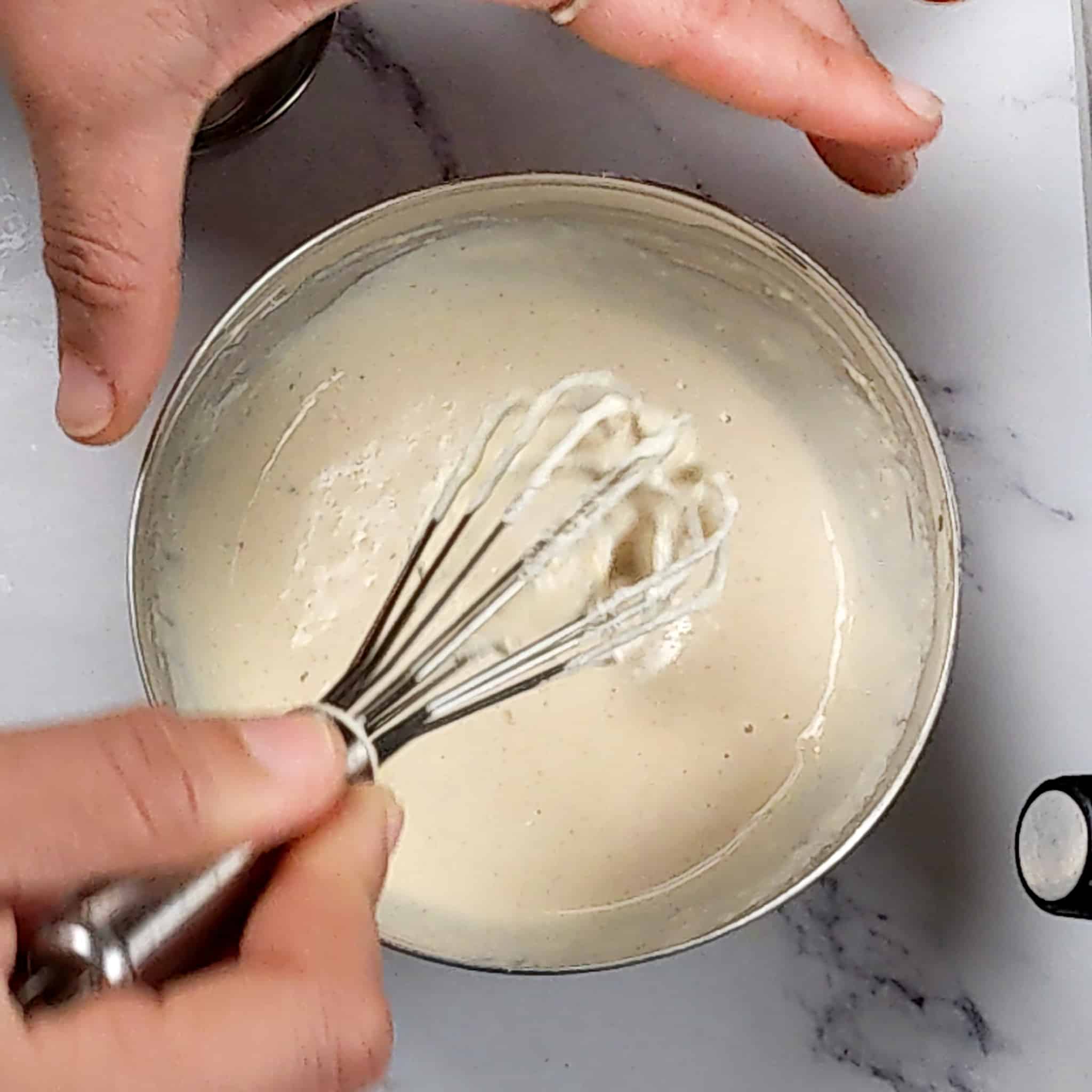 lemon tahini dressing in a small stainless steel mixing bowl with the mini spatula being lifted out.