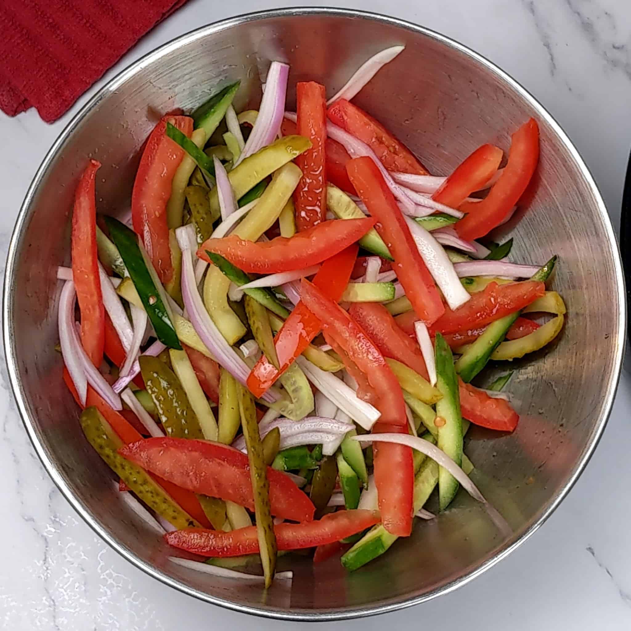 stainless steel mixing bowl with sliced strips of seeded roma tomatoes, pickles, shallots and cucumber.