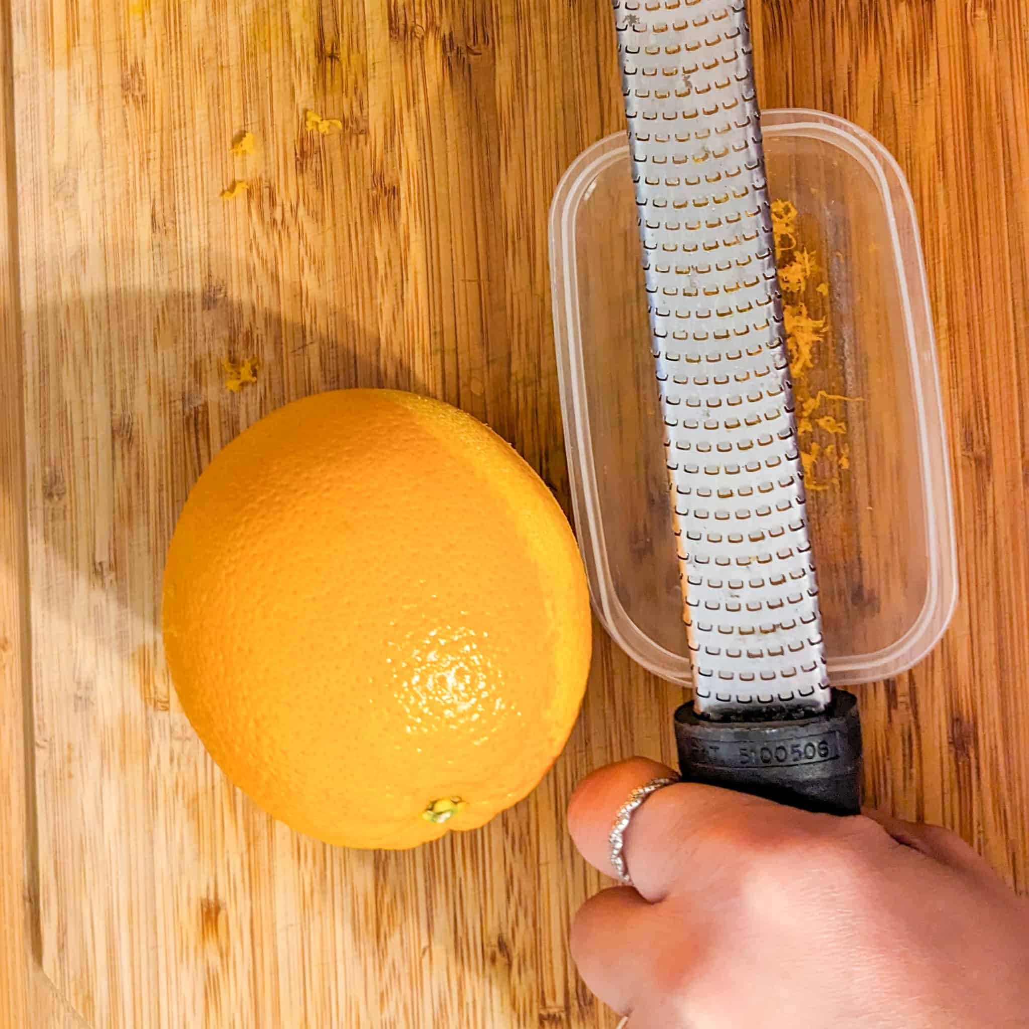 microplane zester on top of a rectangle plastic container catching the zests from an orange that is laying next to it