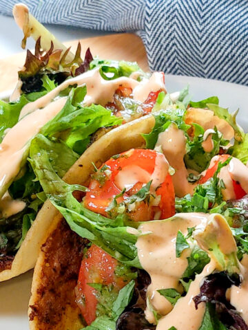 side view and close up the Easy Spicy Crispy Chicken Tacos with Cholula Sour Cream dish on a flat white round plate with shallow straight sides.