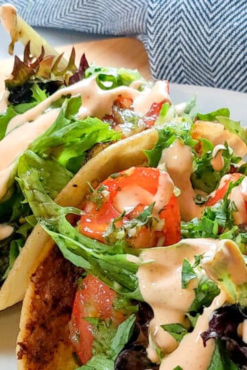 side view and close up the Easy Spicy Crispy Chicken Tacos with Cholula Sour Cream dish on a flat white round plate with shallow straight sides.