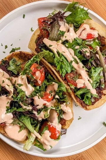 top view of the the Easy Spicy Crispy Chicken Tacos with Cholula Sour Cream sprinkled with fresh chopped cilantr on a flat white round plate with shallow straight sides.