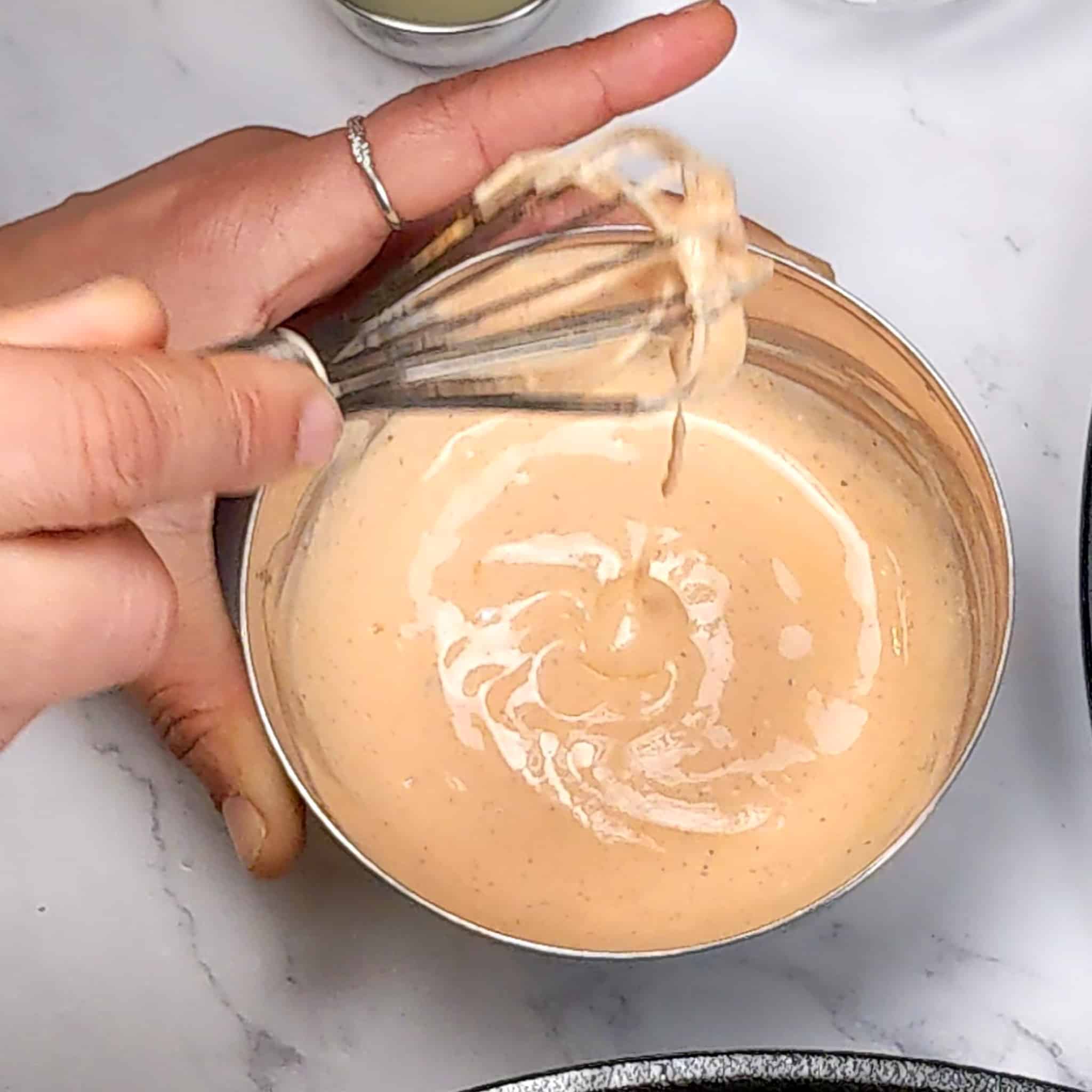a whisk lifted up from the creamy Cholula sour cream sauce in a small stainless steel bowl.