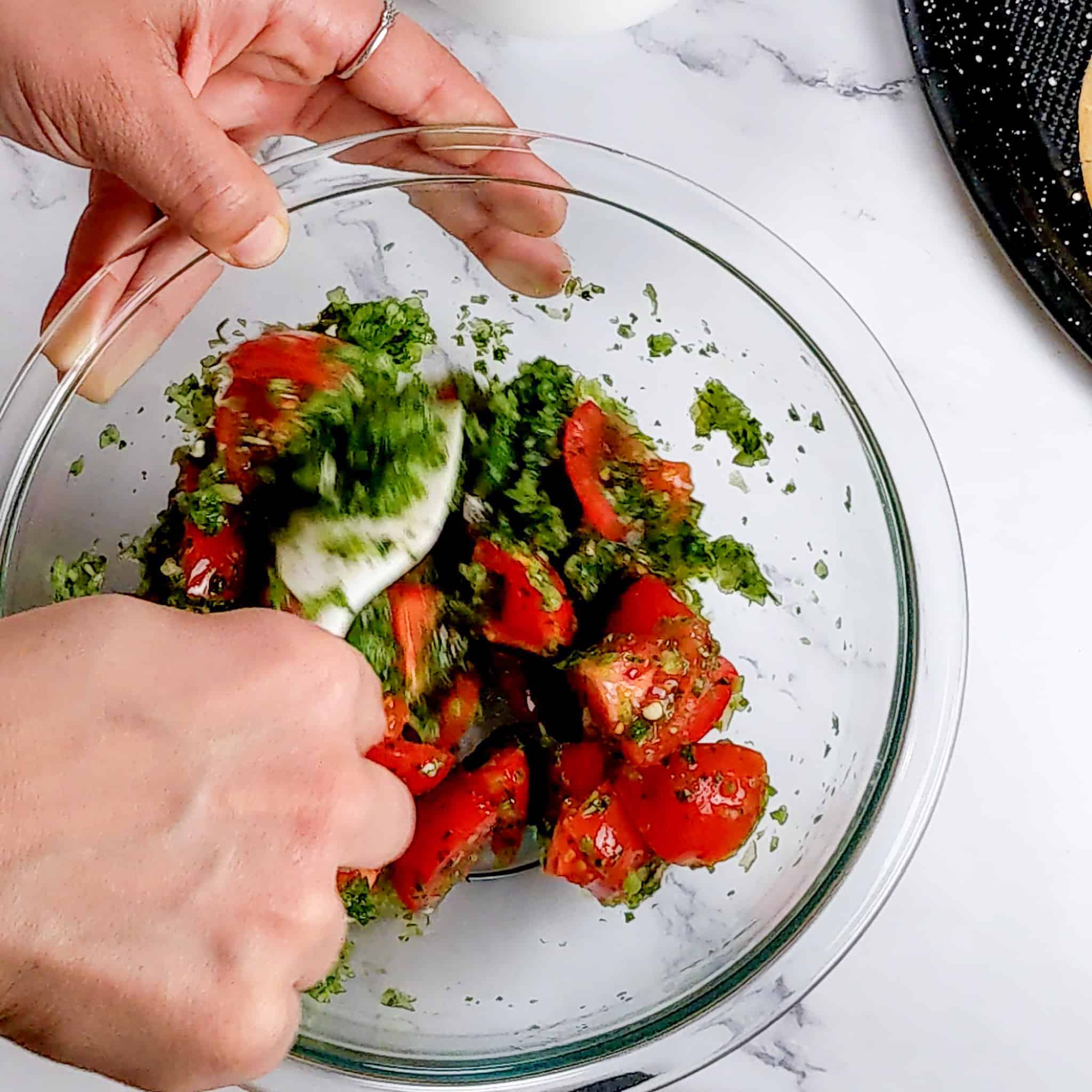 quartered campari tomatoes and aromatic paste being mixed in a glass mixing bowl with a silicone spatula