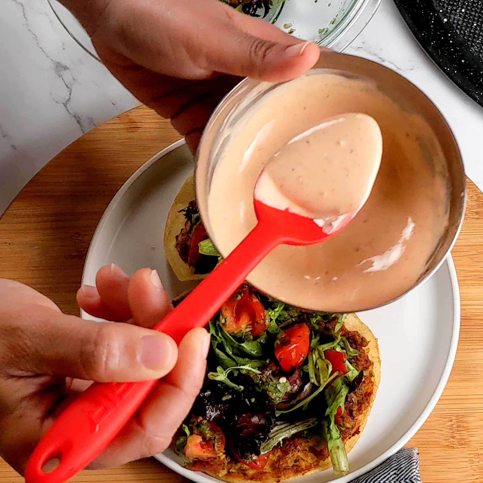 The cholula sour cream on a silicone spoon over a bowl of the sauce in a stainless mini bowl over the plated crispy chicken tacos