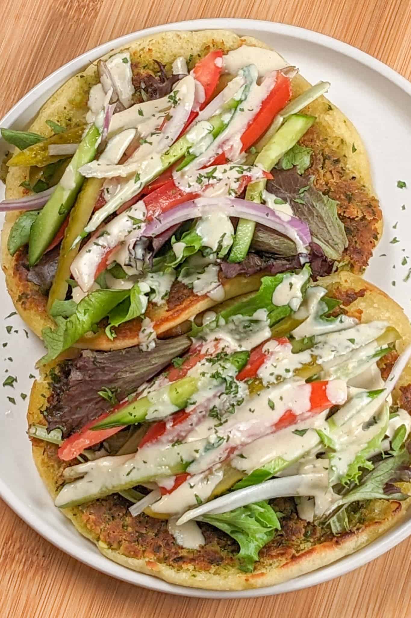 Two Spicy Falafel Pita Sandwiches with Lemon Tahini Dressing on a round white plate.