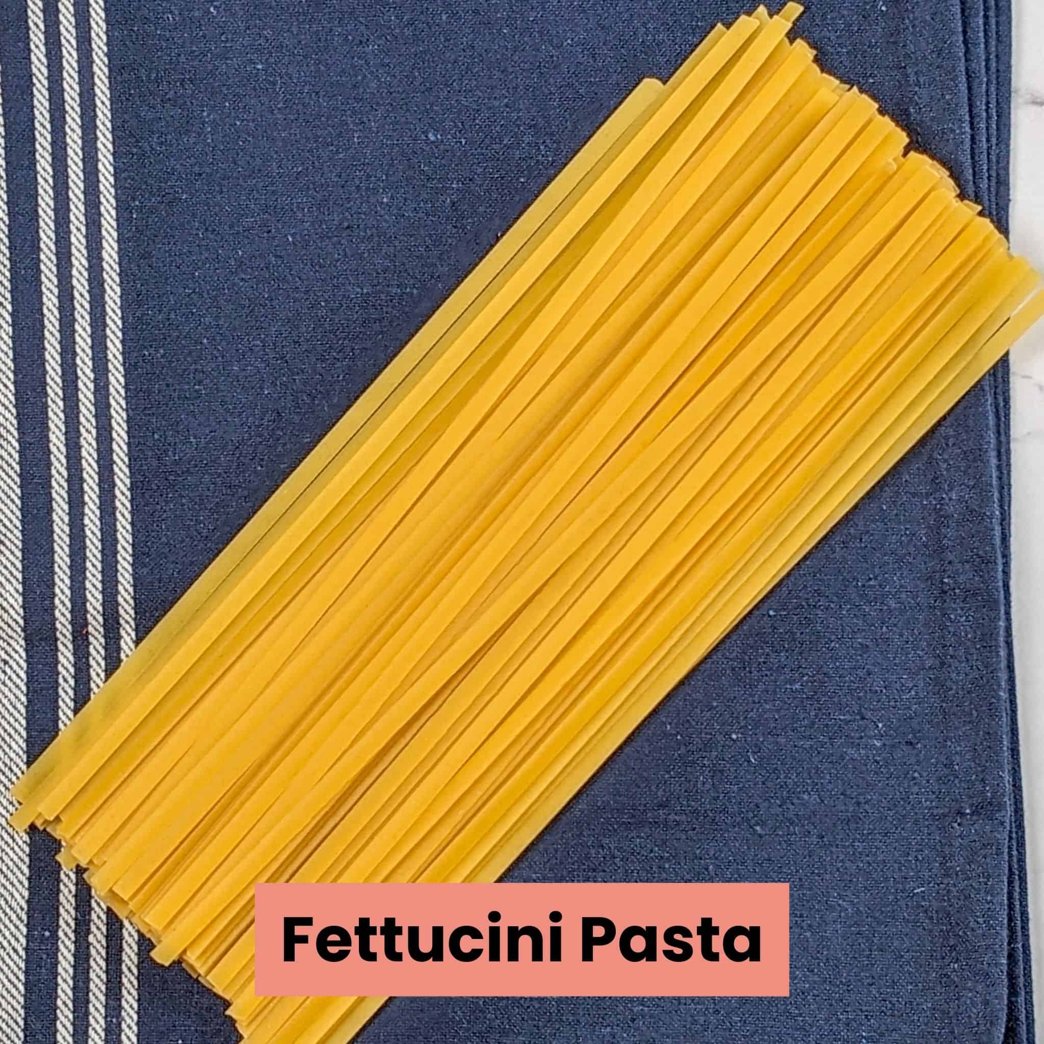 raw dry fettuccini pasta pile in an even layer on a kitchen towel.