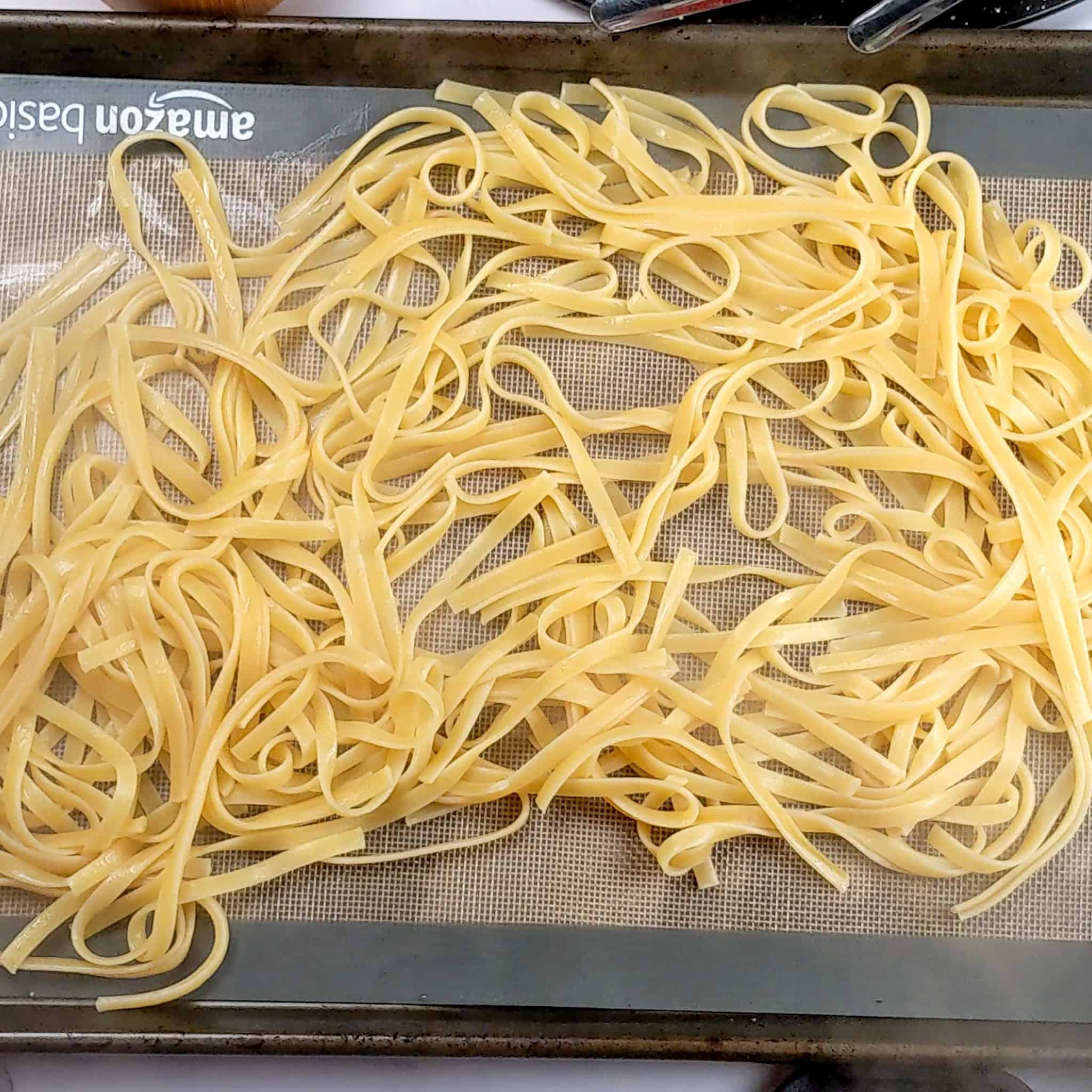 al dente fettuccini pasta spread out on a silicone mat lined baking sheet pan.