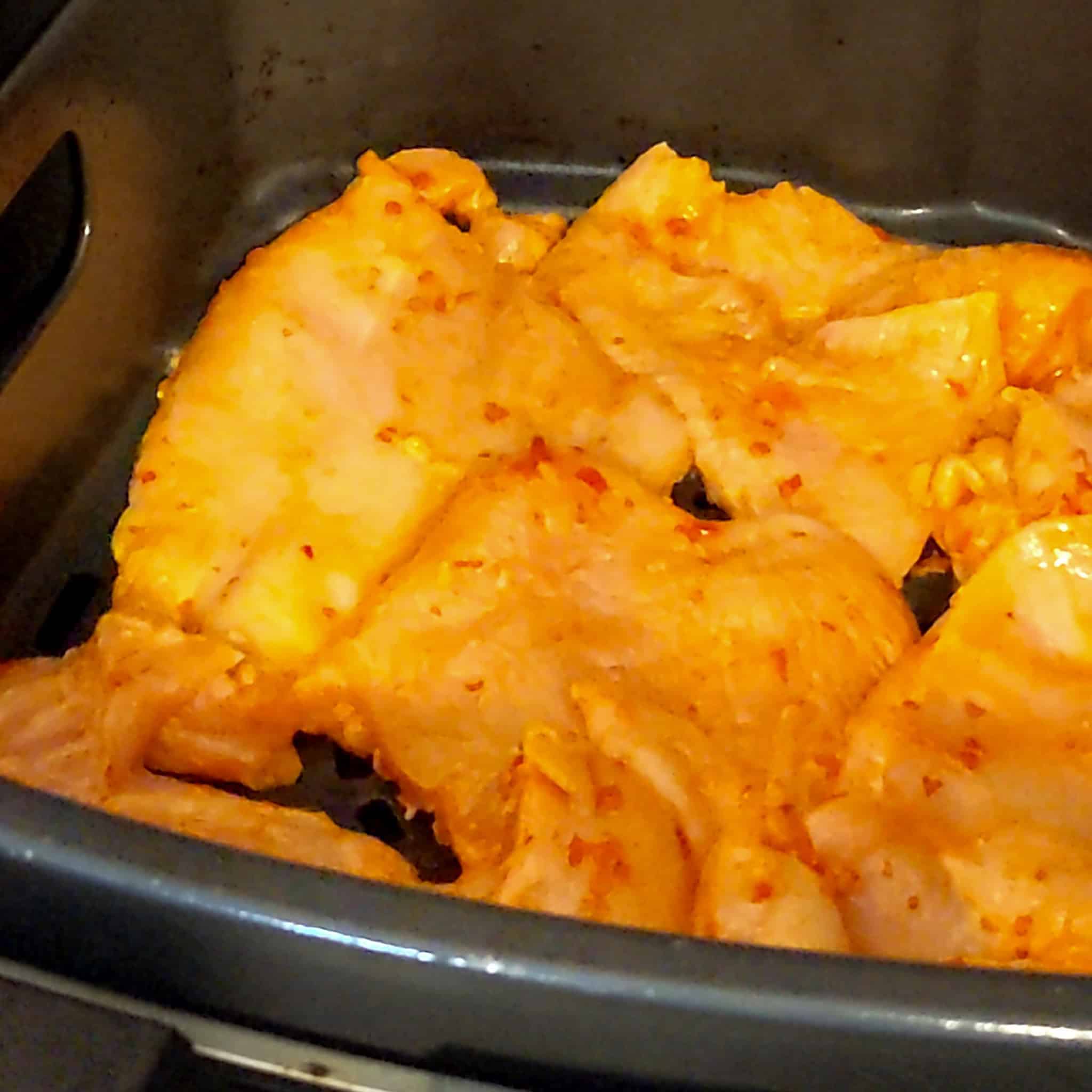 garlic chili sauce marinaded chicken cutlets in an air fryer basket.