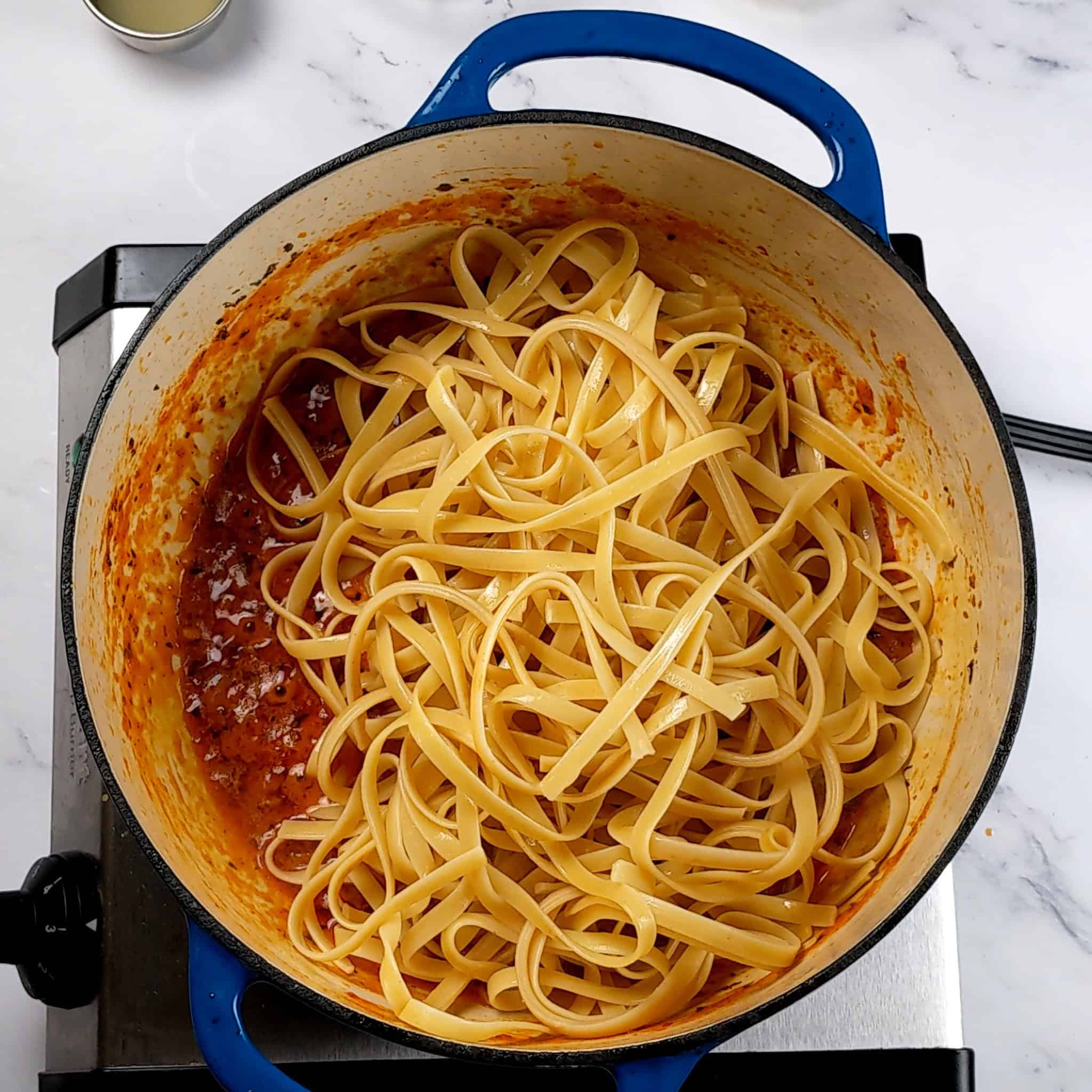 cooked fettuccini pasta on top of the garlic chili sauce coconut curry pasta sauce in a dutch oven.