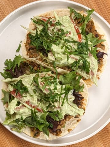 top view of two Salsa Verde Turkey and Beans Tacos with Avocado Cream on a white round plate with shallow sides on a wooden lazy susan.