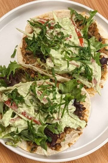 top view of two Salsa Verde Turkey and Beans Tacos with Avocado Cream on a white round plate with shallow sides on a wooden lazy susan.