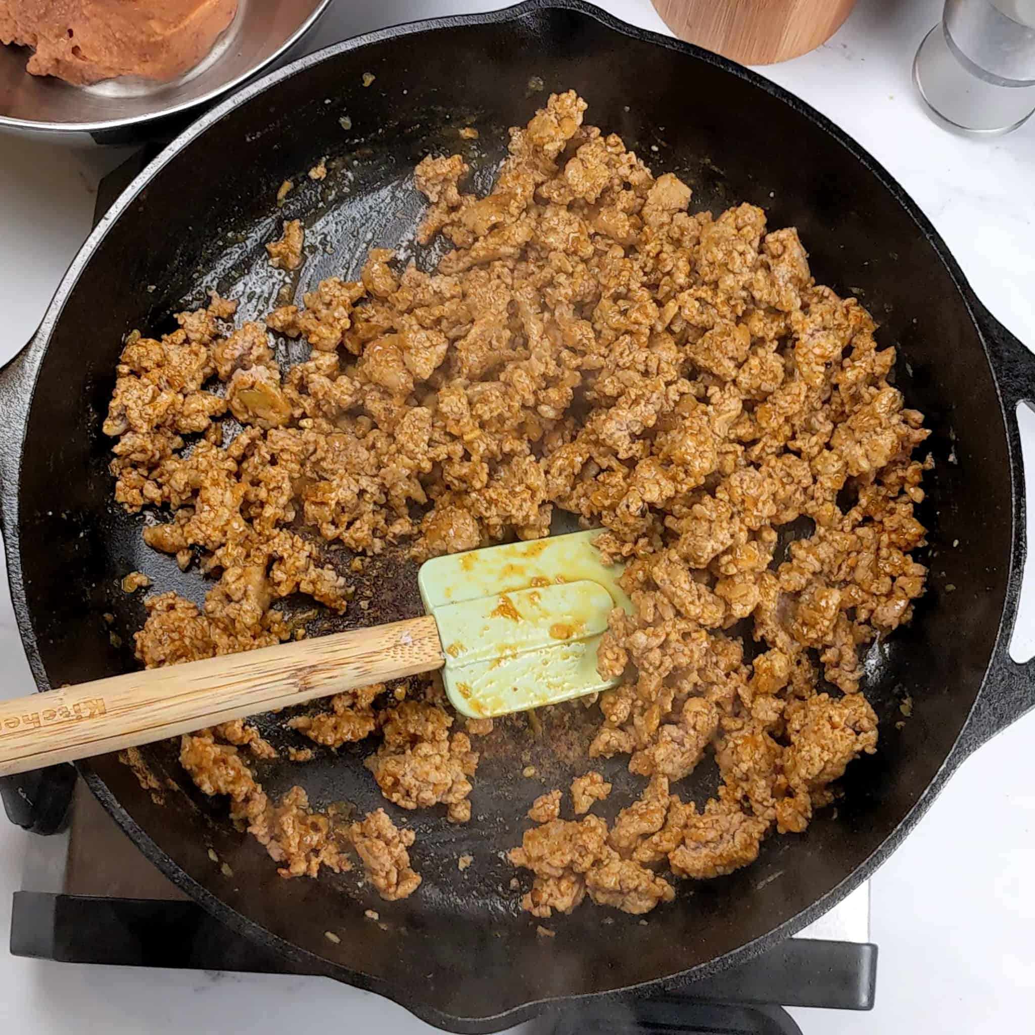 seasoned cooked crumbled ground turkey in a cast iron skillet with a silicone kitchenaid silicon cone and wooden handle spatula.
