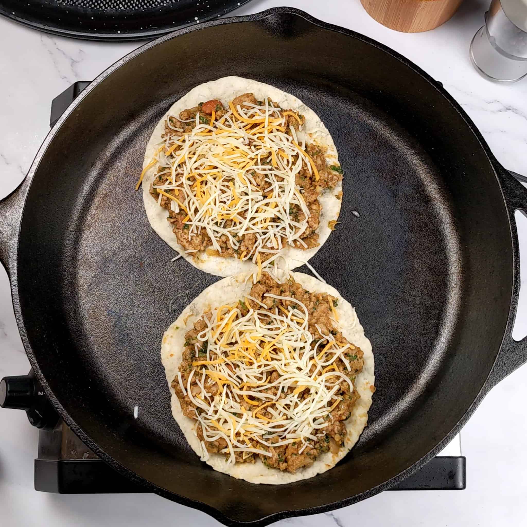 Salsa Verde Turkey and Beans Tacos facing meat side up in a lodge cast iron skillet with shredded mexican cheese blend sprinkled on top of each.