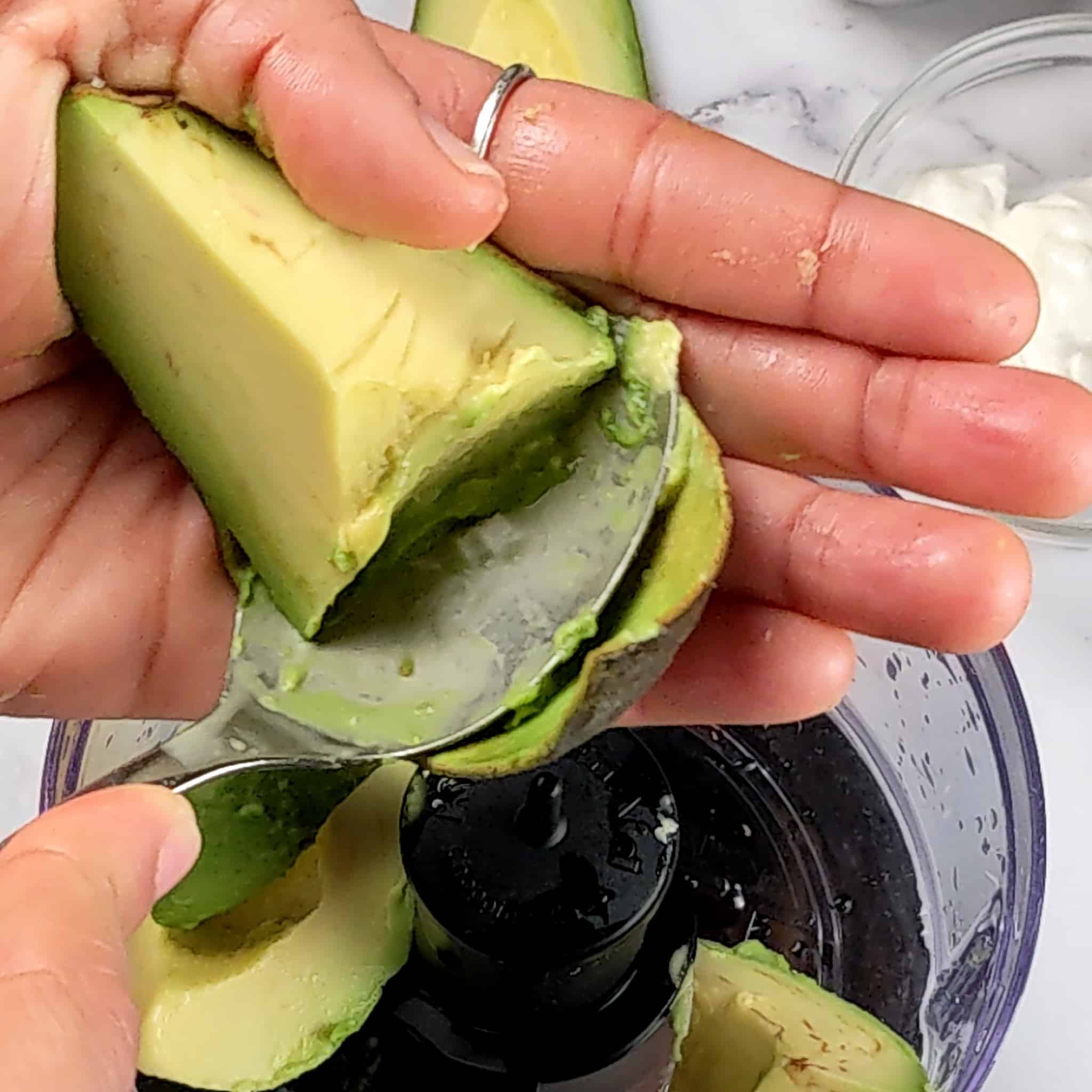 a quartered ripe avocado meat being spooned out of it's skin over an open food processor.