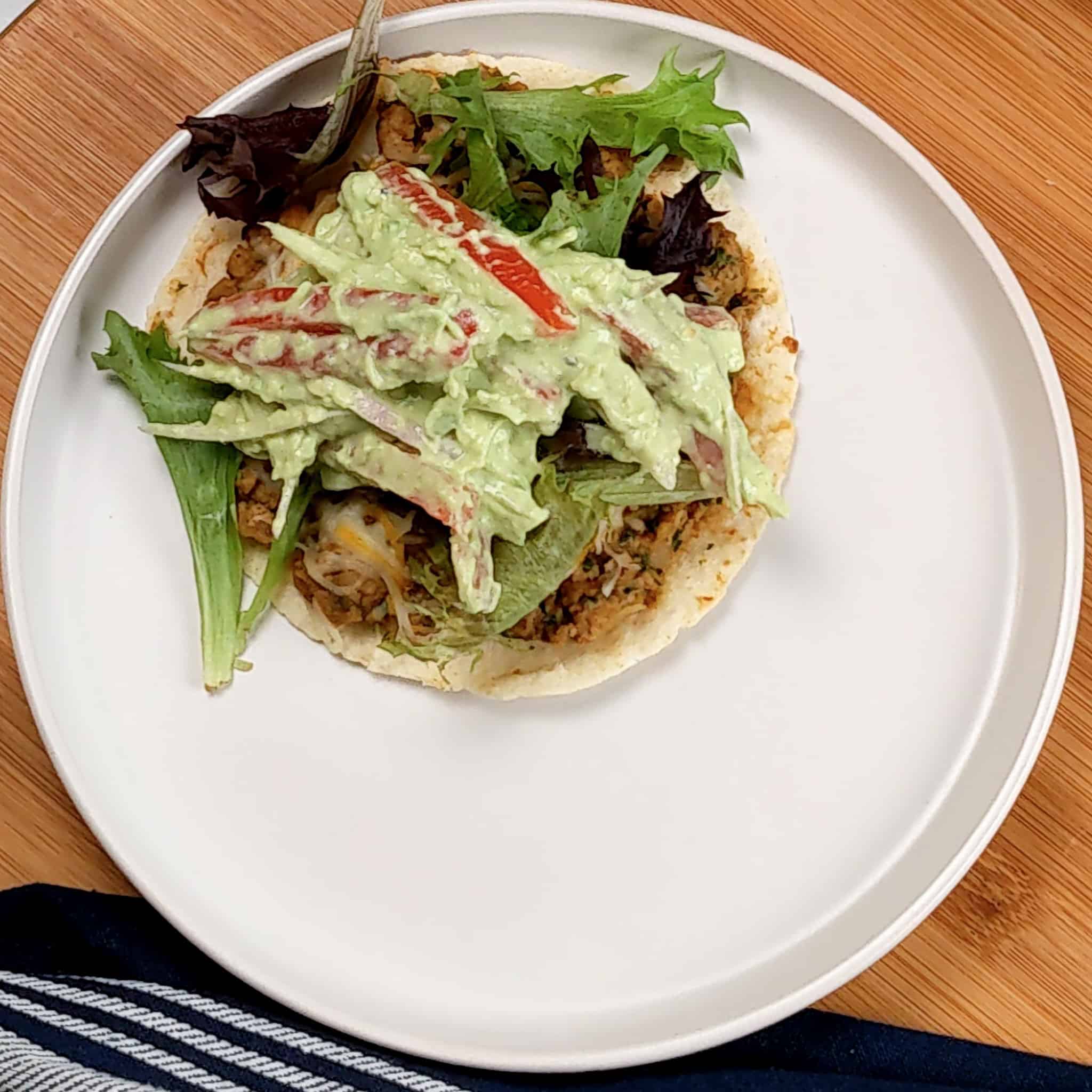one flour tortilla packed with cooked seasoned ground turkey and refried beans and melted cheese, topped with mixed greens, and avocado cream tomato salad.