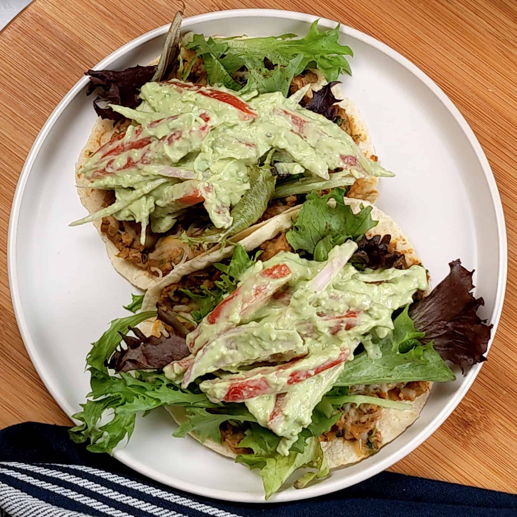two flour tortillas packed with cooked seasoned ground turkey and refried beans and melted cheese, topped with mixed greens, and avocado cream tomato salad on a round flat plate with shallow straight sides.
