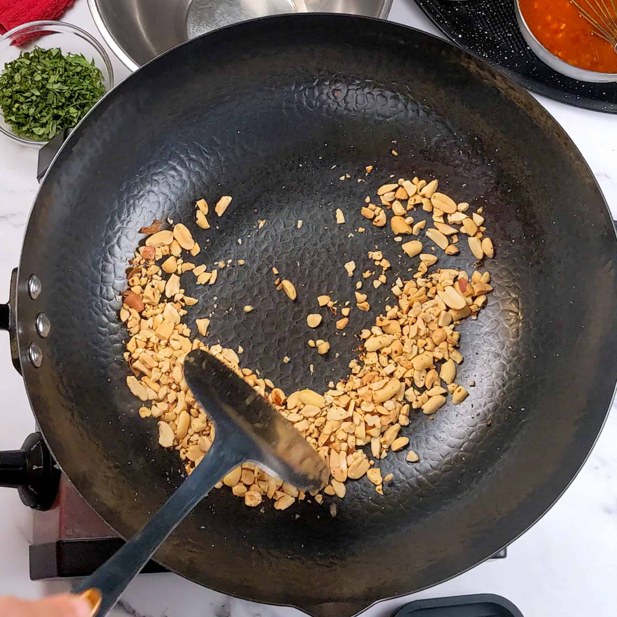 crushed peanuts toasting in a wok while being stirred with a wok spatula.