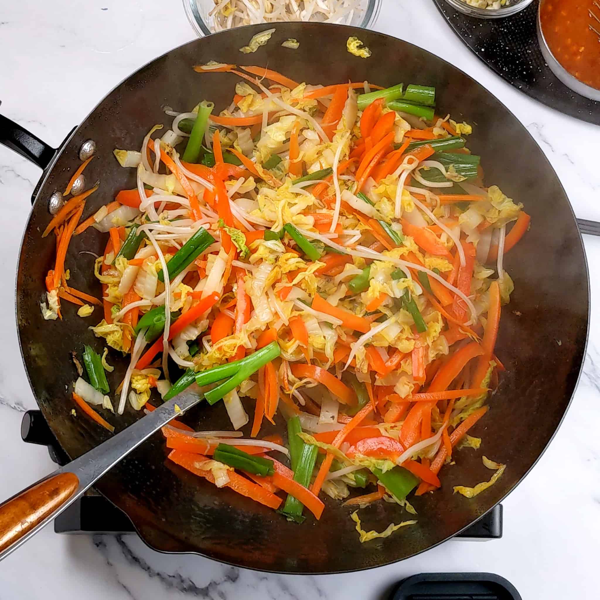 vivid cooked red bell pepper, scallions, bean sprouts, nappa cabbage and carrots in a wok.