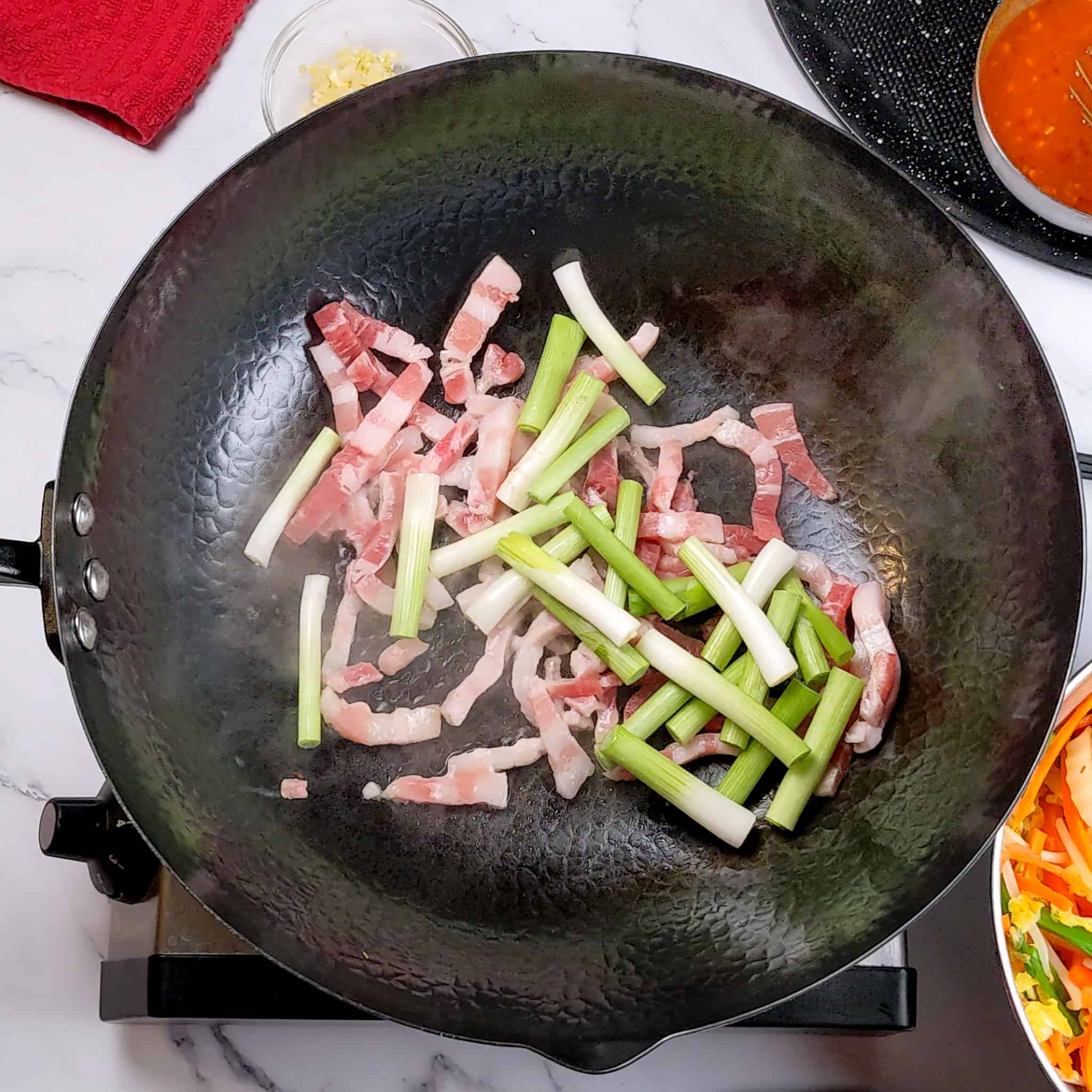 1-inch scallions and thin strips of pork belly stir-frying in a wok.