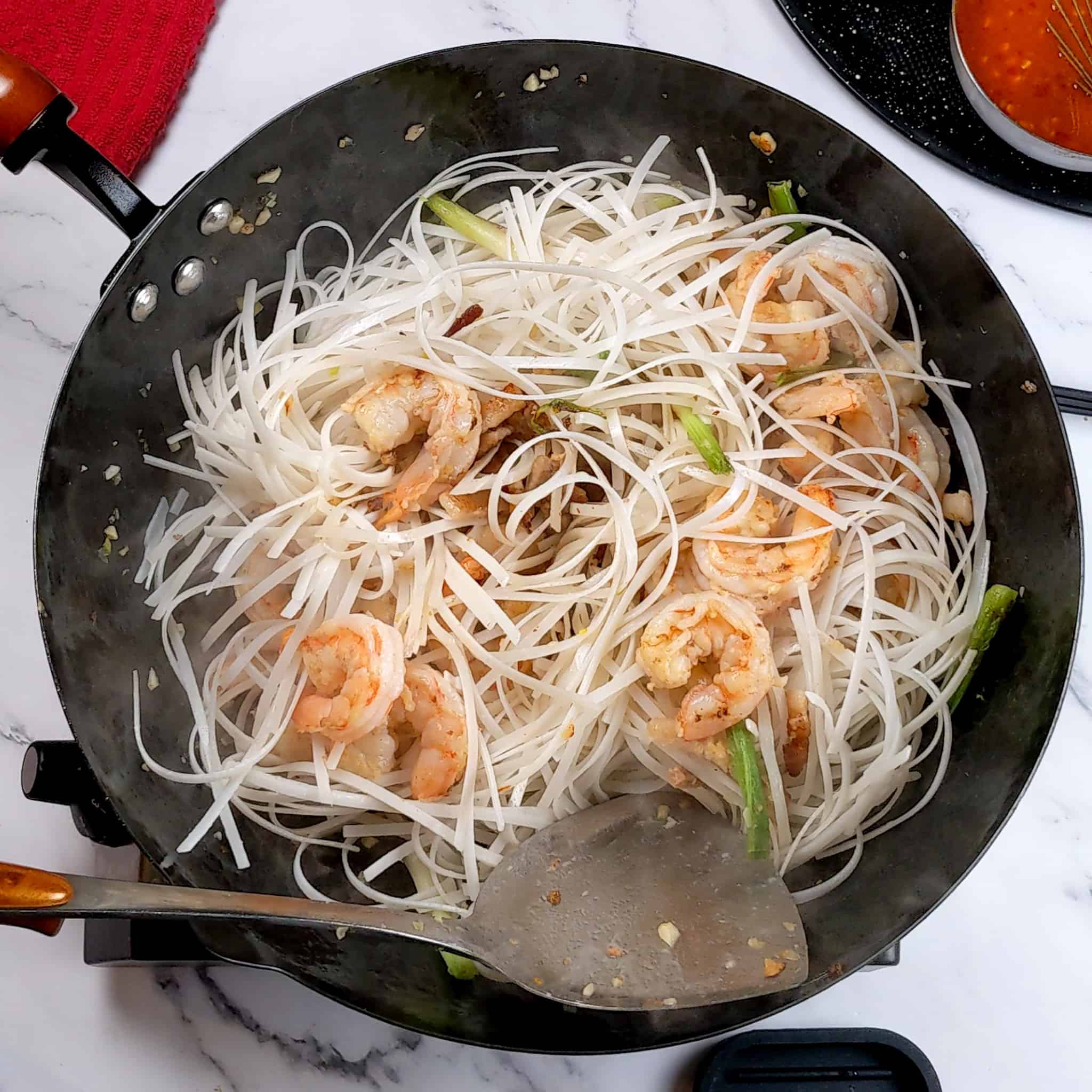 raw soaked pad thai noodles added to the shrimp and scallion mixture stir-fry in a wok.