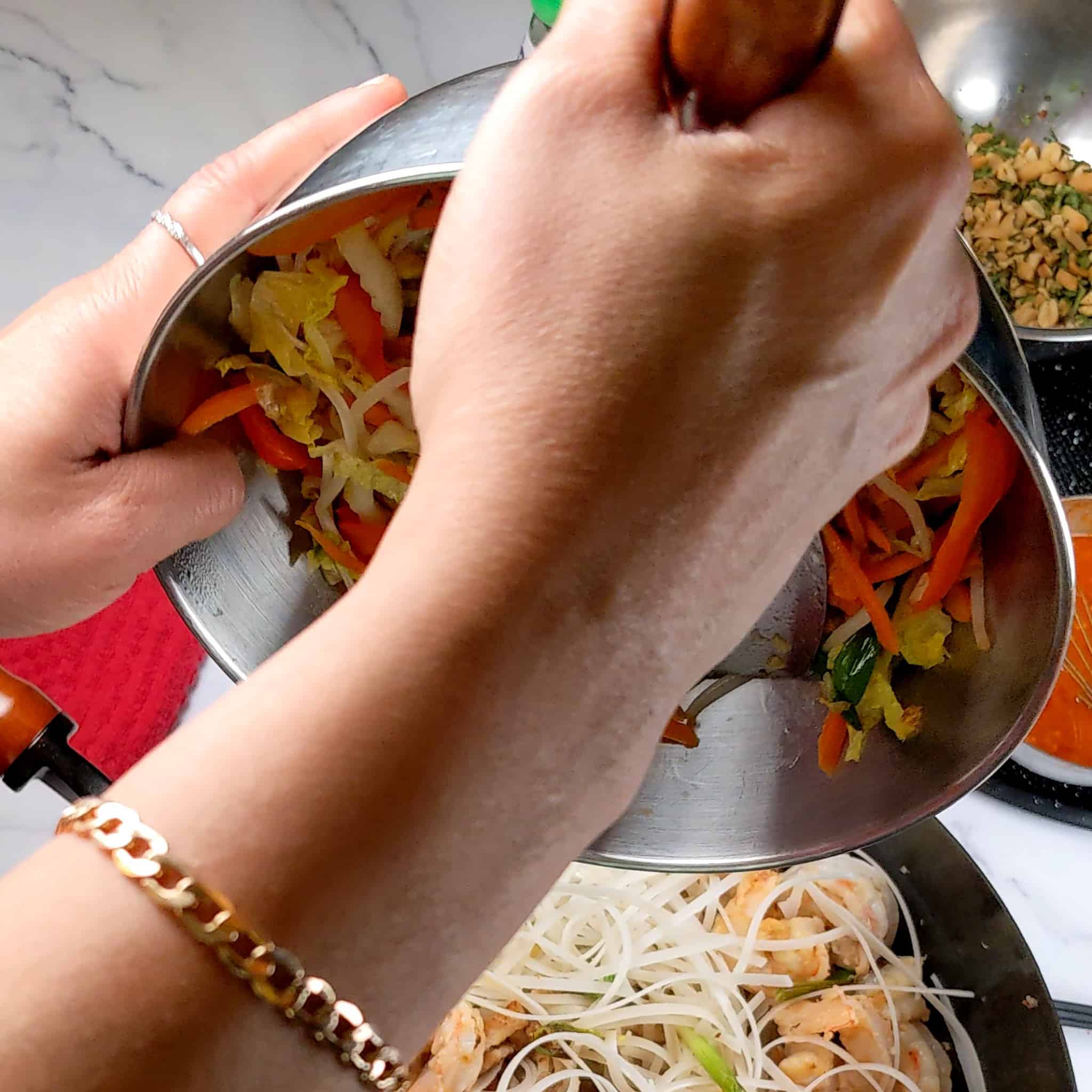 liquid from the sautéed vegetables being poured into the noodles and shrimp.