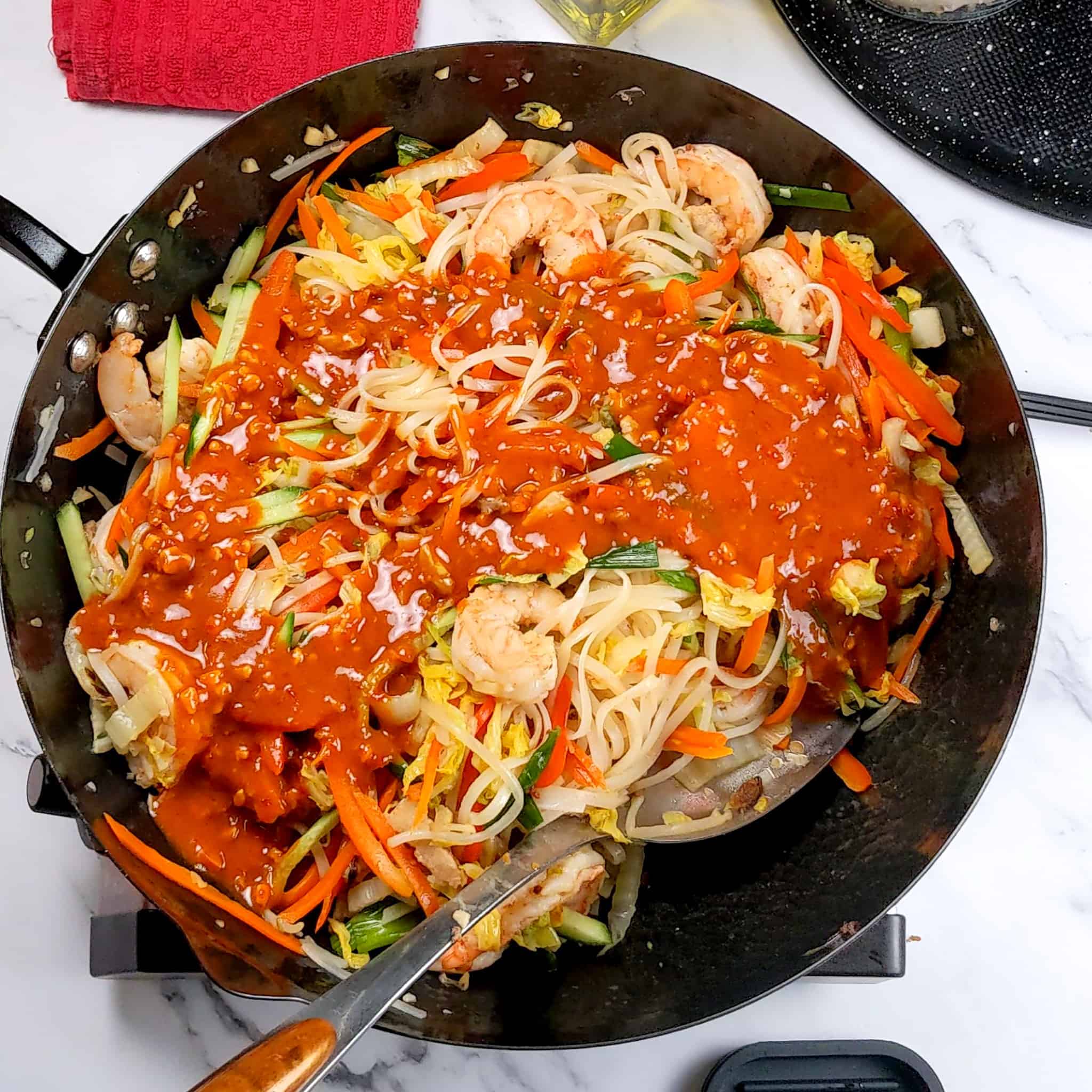 garlic chili peanut sauce poured on top of the shrimp and pork belly pad thai in the wok.