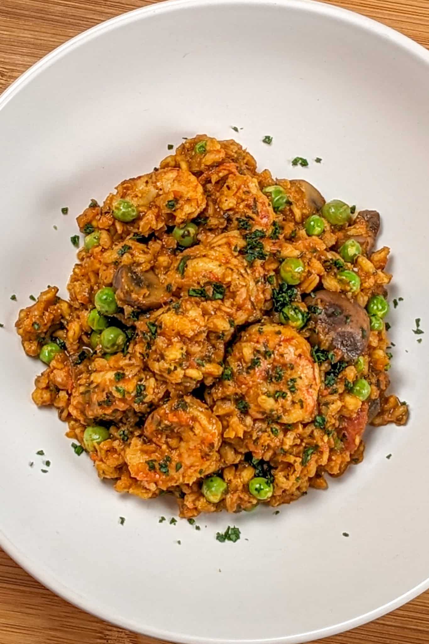 The Spicy Shrimp Farro Risotto with Mushrooms and Peas recipe in a wide rim bowl garnished with chopped parsley