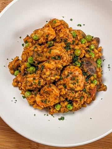 The Spicy Shrimp Farro Risotto with Mushrooms and Peas recipe in a wide rim bowl garnished with chopped parsley