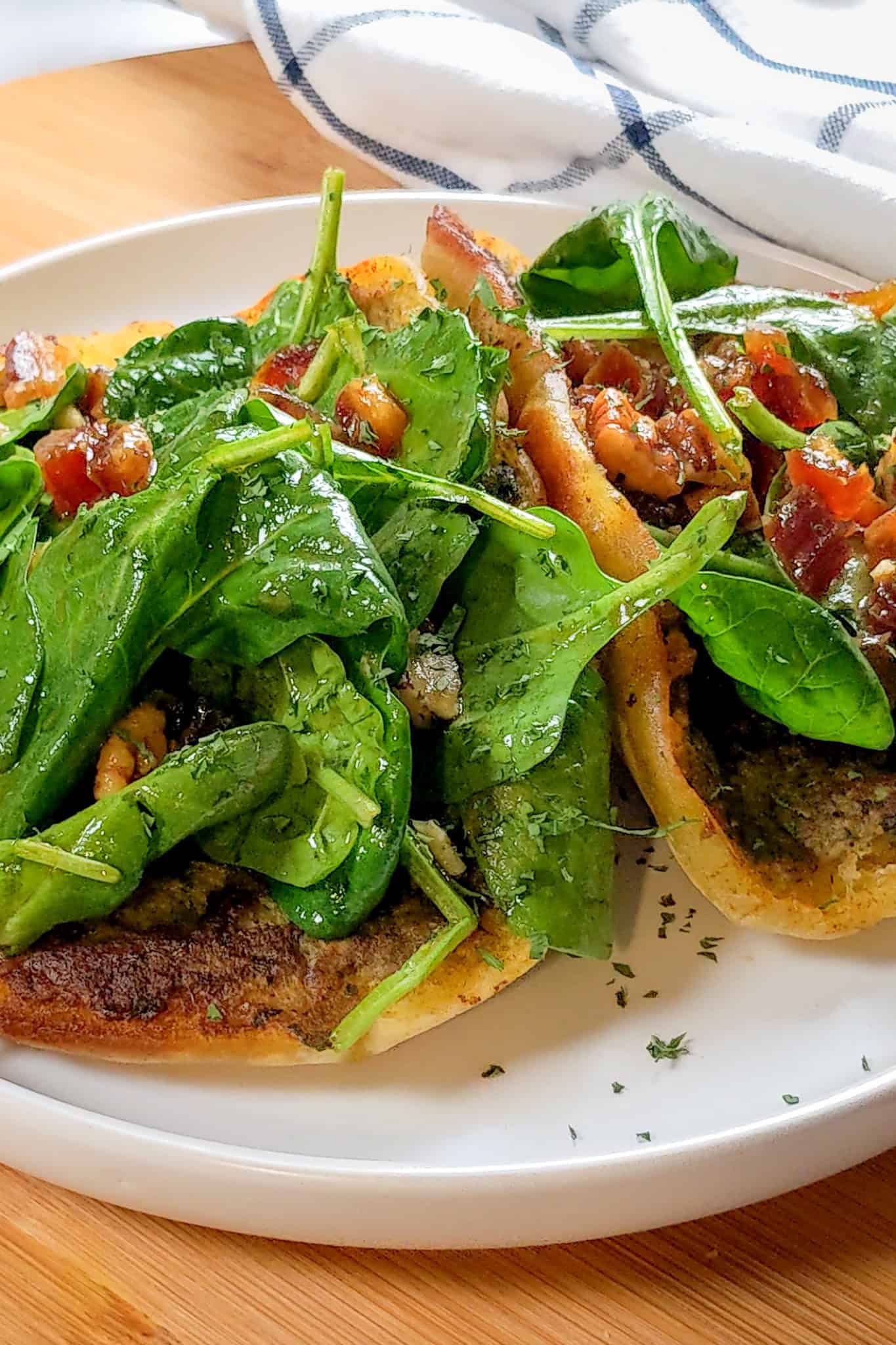 pan-fried pita bread with a layer of cooked zhug spiced ground chicken topped with spinach in a pomegranate vinaigrette with dates and pecans on a round plate with shallow straight sides.
