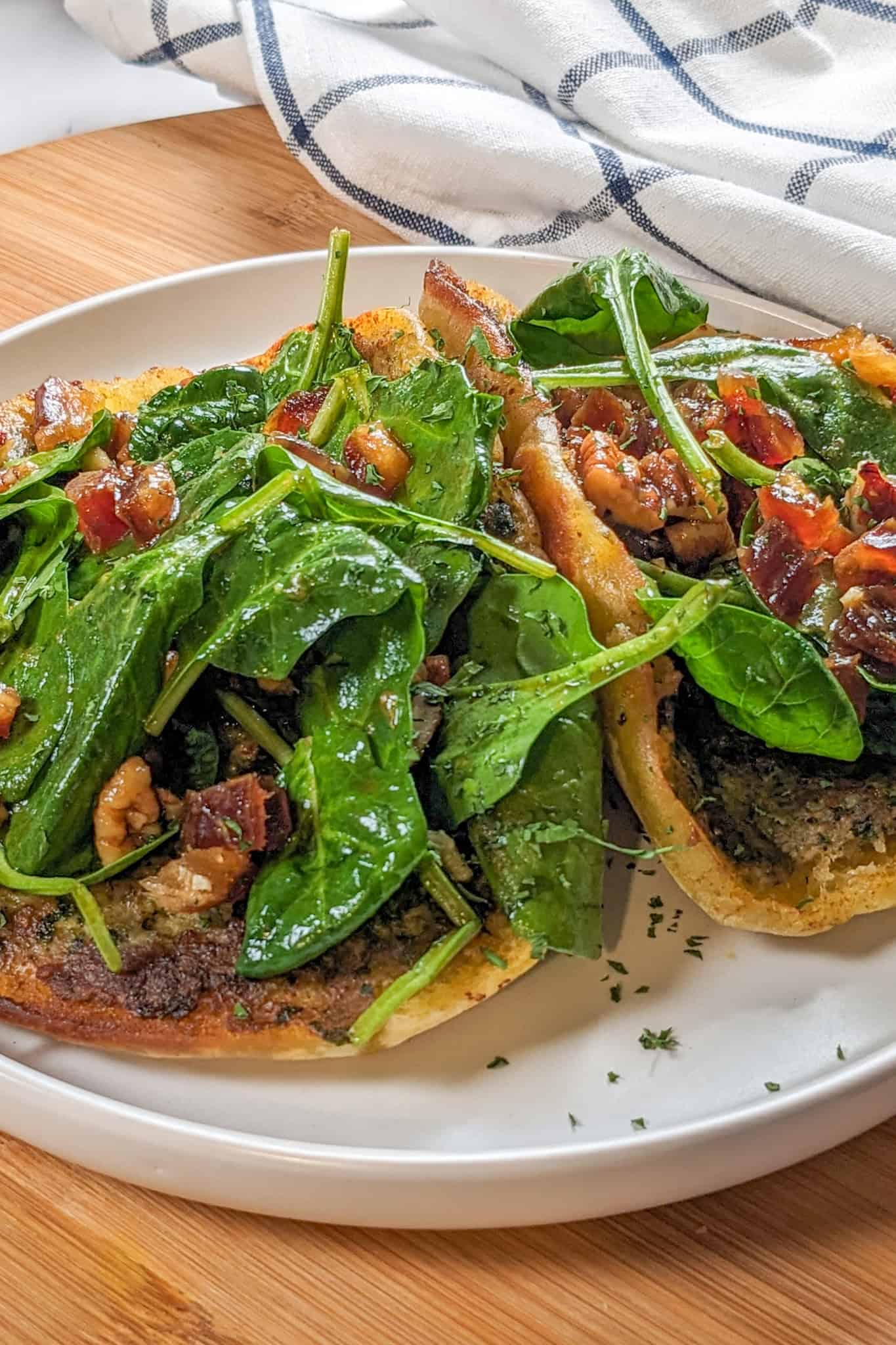 pan-fried pita bread with a layer of cooked zhug spiced ground chicken topped with spinach in a pomegranate vinaigrette with dates and pecans on a round plate with shallow straight sides.