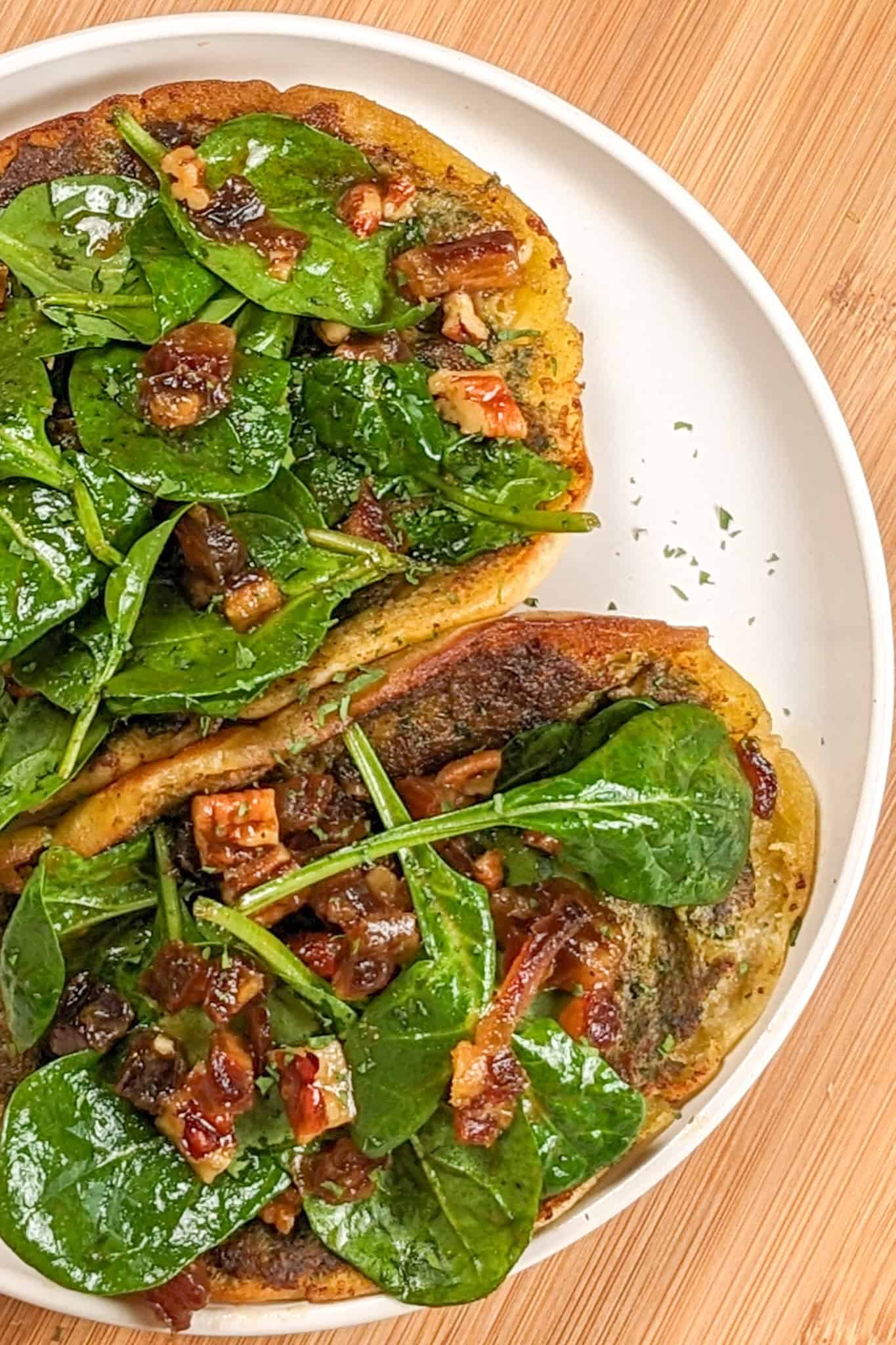 pan-fried pita bread with a layer of cooked zhug spiced ground chicken topped with spinach in a pomegranate vinaigrette with dates and pecans on a round plate with shallow straight sides.