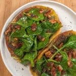 pan-fried pita bread with a layer of cooked zhug spiced ground chicken topped with spinach in a pomegranate vinaigrette with dates and pecans on a round plate with shallow straight sides.