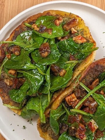 pan-fried pita bread with a layer of cooked zhug spiced ground chicken topped with spinach in a pomegranate vinaigrette with dates and pecans on a round plate with shallow straight sides.