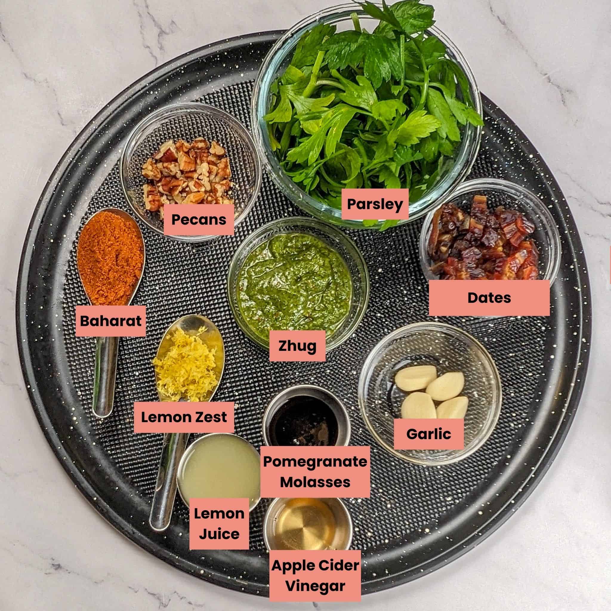 ingredients for the spicy zhug chicken pita sandwiches on a large round pizza pan in glass and stainless steel containers.