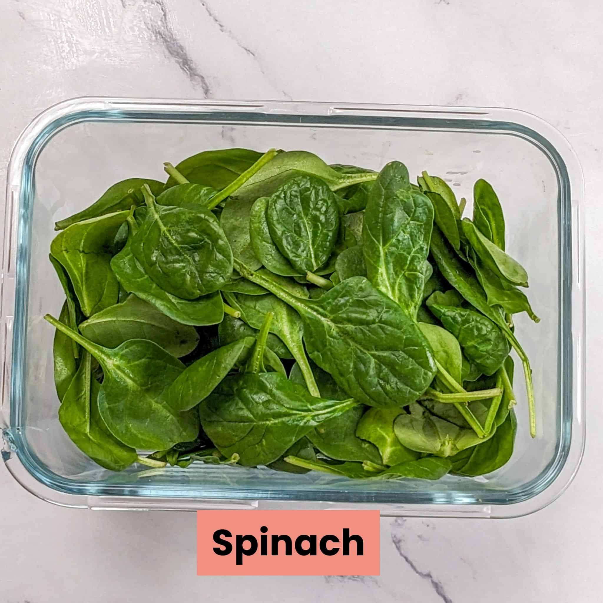 fresh baby spinach in a deep glass rectangle container.